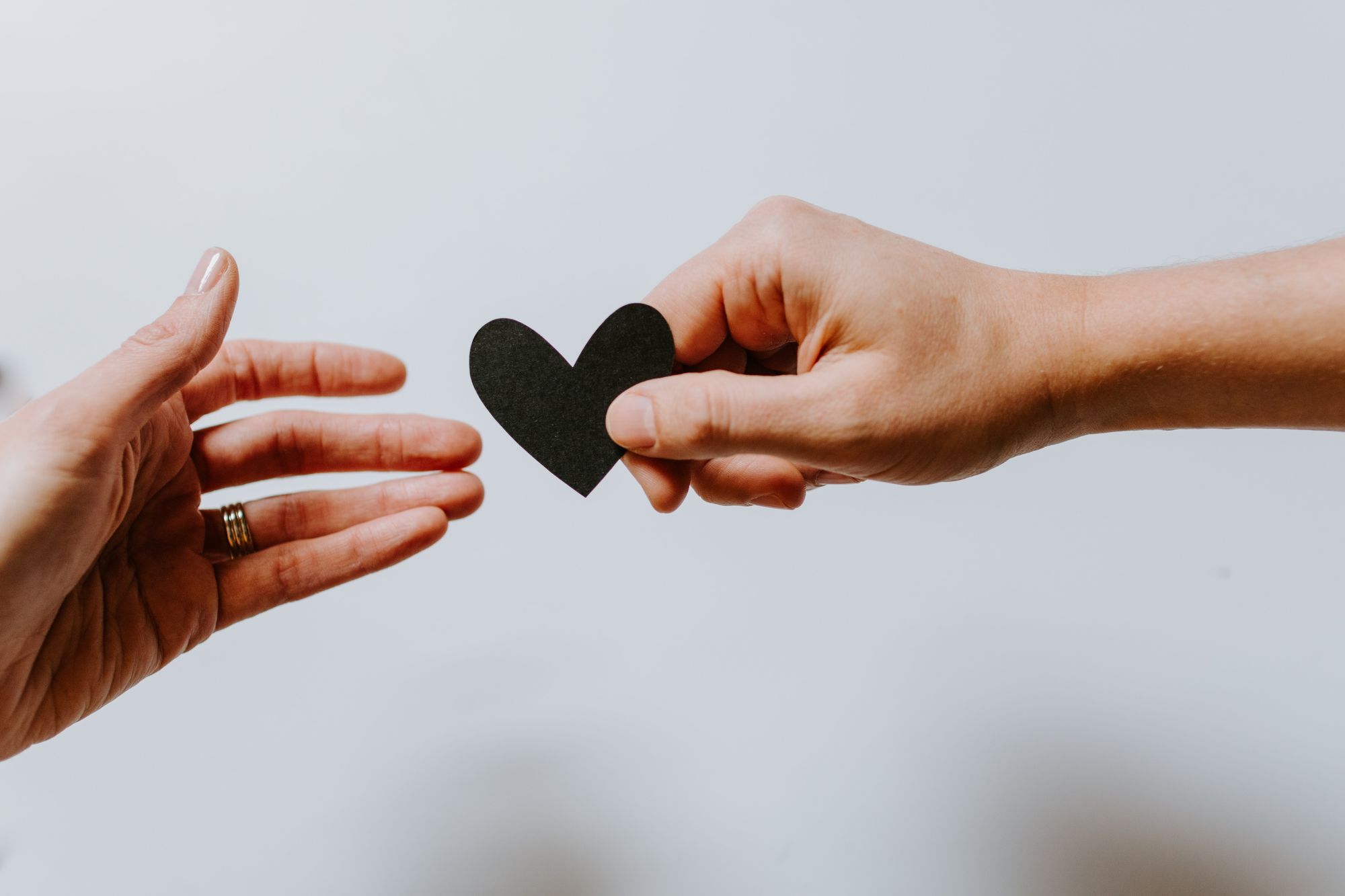 A woman passes another woman a paper heart.